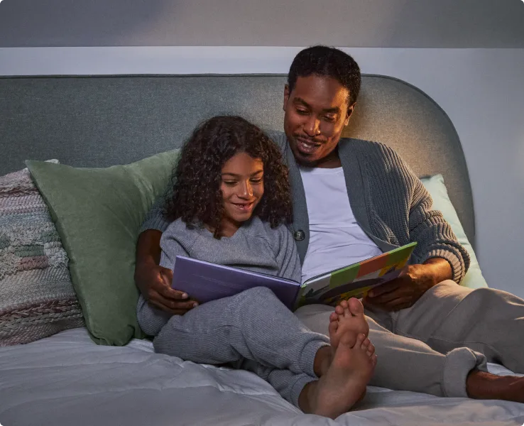 A father and daughter read a bedtime story together while an energy-efficient smart LED bulb lights up the bedroom.