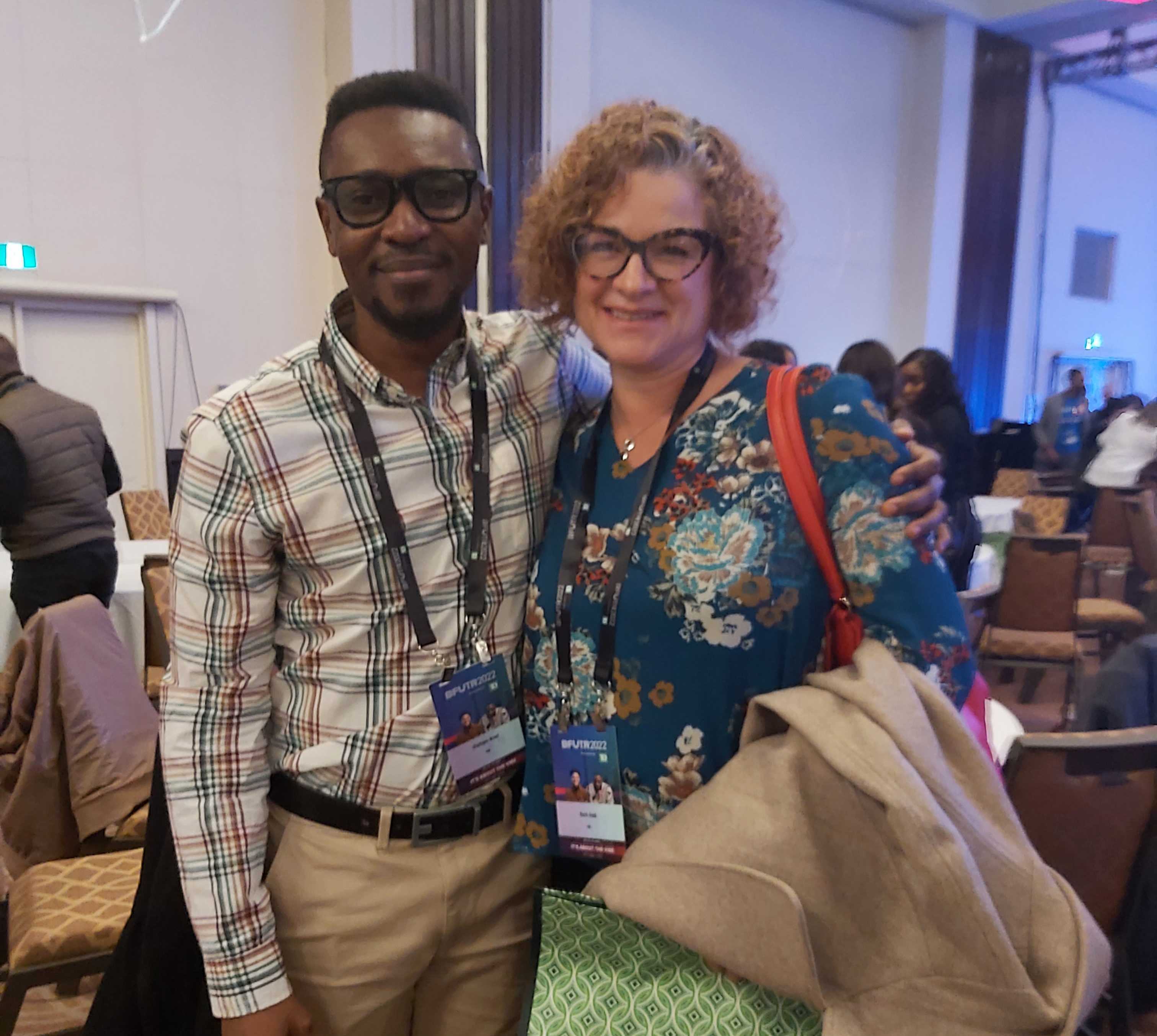 Two black team members pose together at a conference, both wearing lanyards