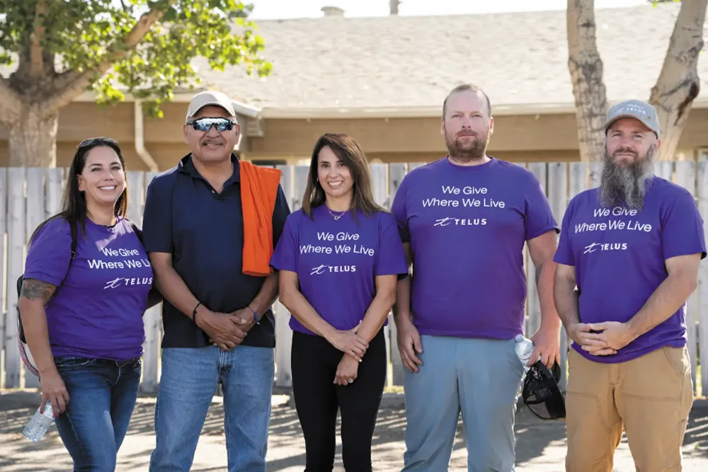 Five community volunteers, four wearing purple TELUS shirts, posing together outdoors in a row.
