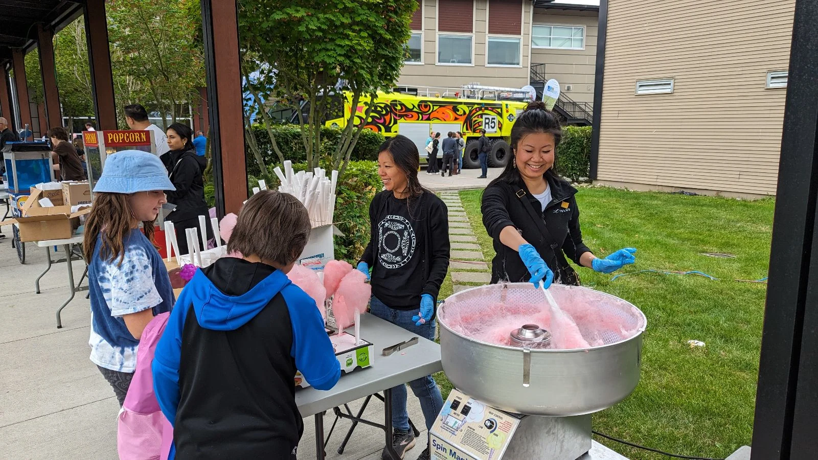 Anne Zhong and a TELUS team member serving two children at the candy cotton stand. 