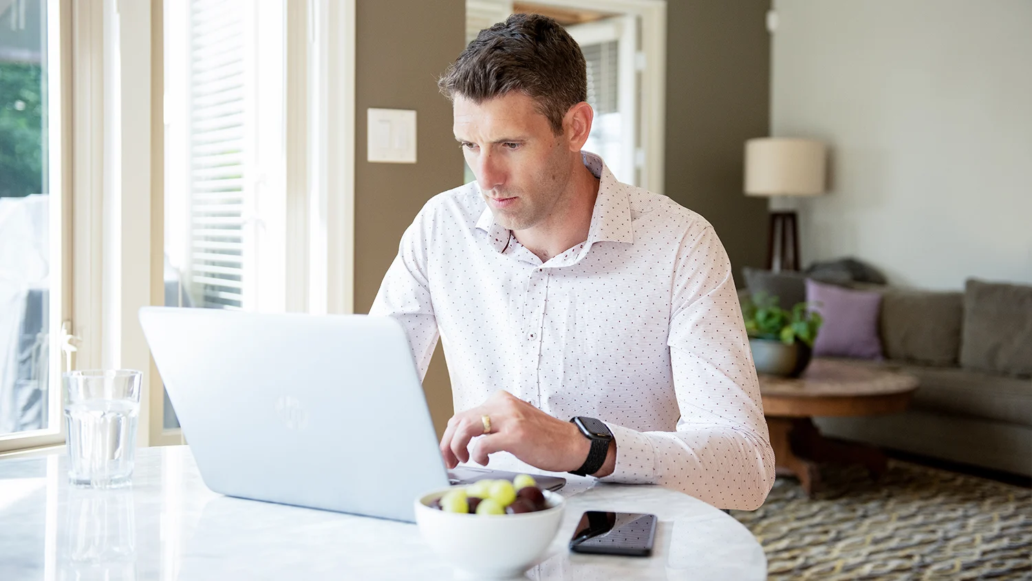 Man typing on a laptop at a kitchen table in a house as he works virtually 