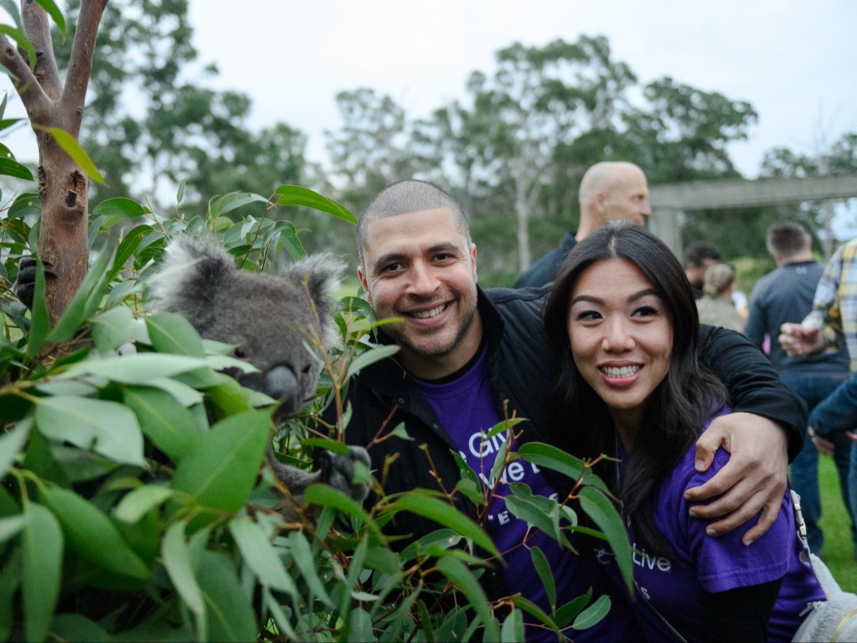 Two TELUS team members smiling next to a koala.

