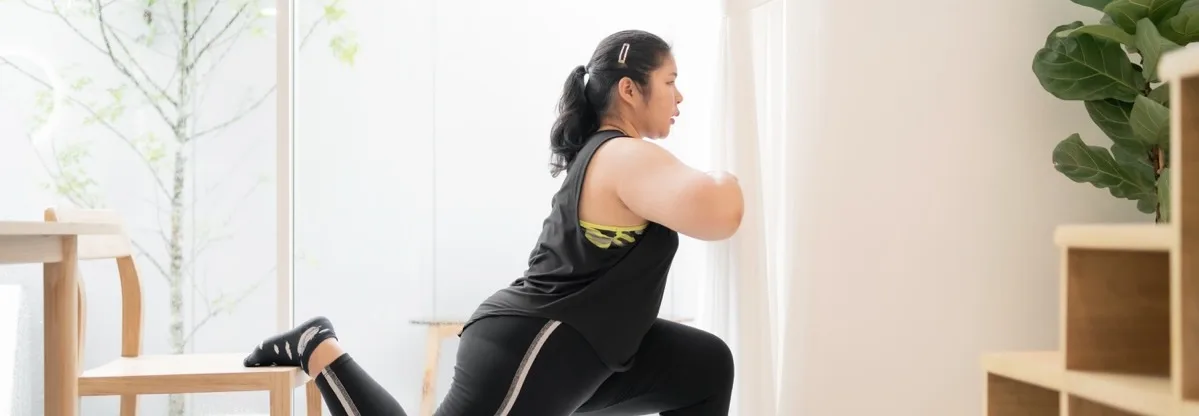 Femme effectuant une fente bulgare en utilisant une chaise en bois pour le soutien dans un espace de fitness minimaliste et lumineux avec des plantes