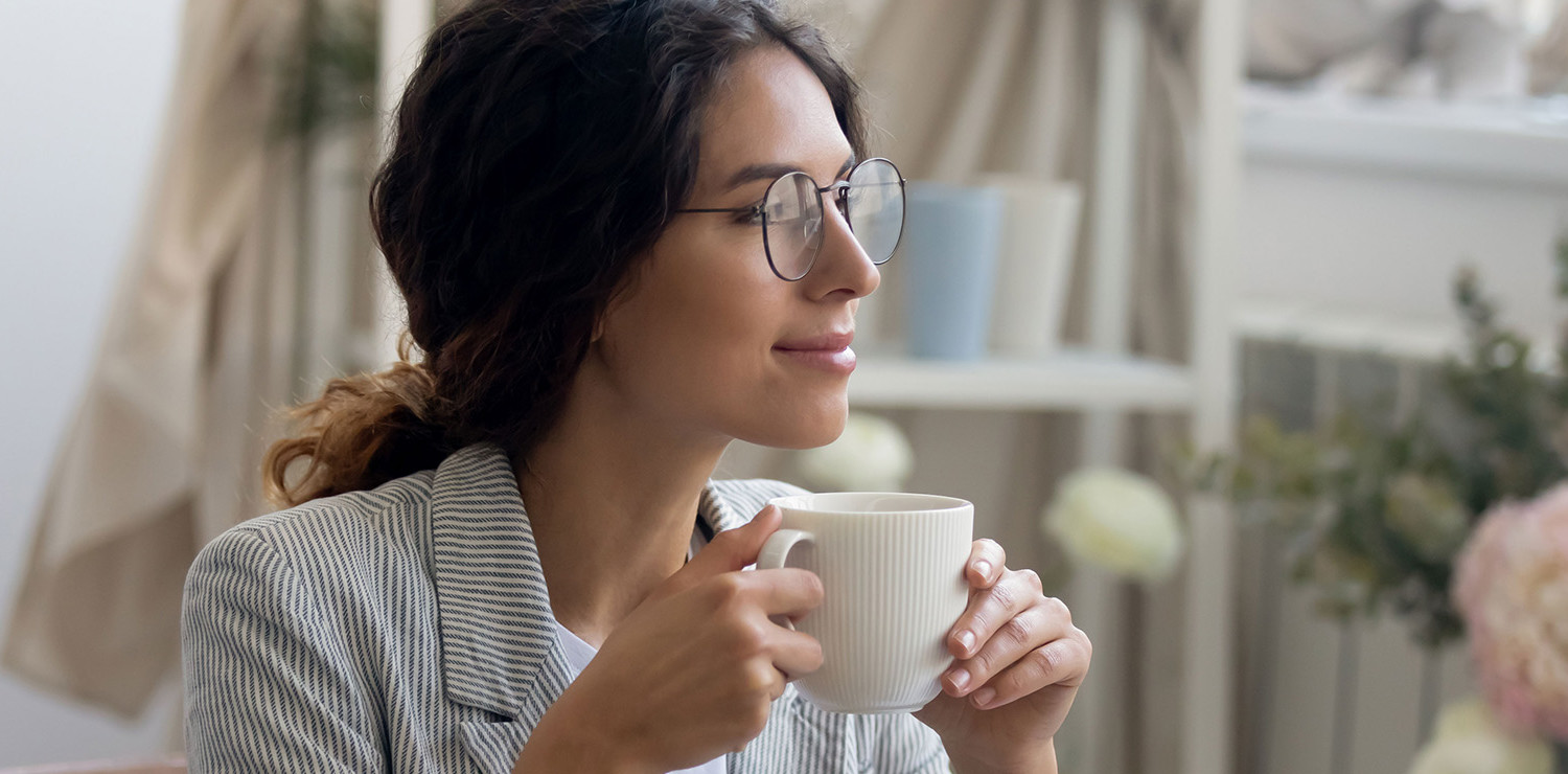 Smiling young business woman with glasses drinks coffee at home in her office