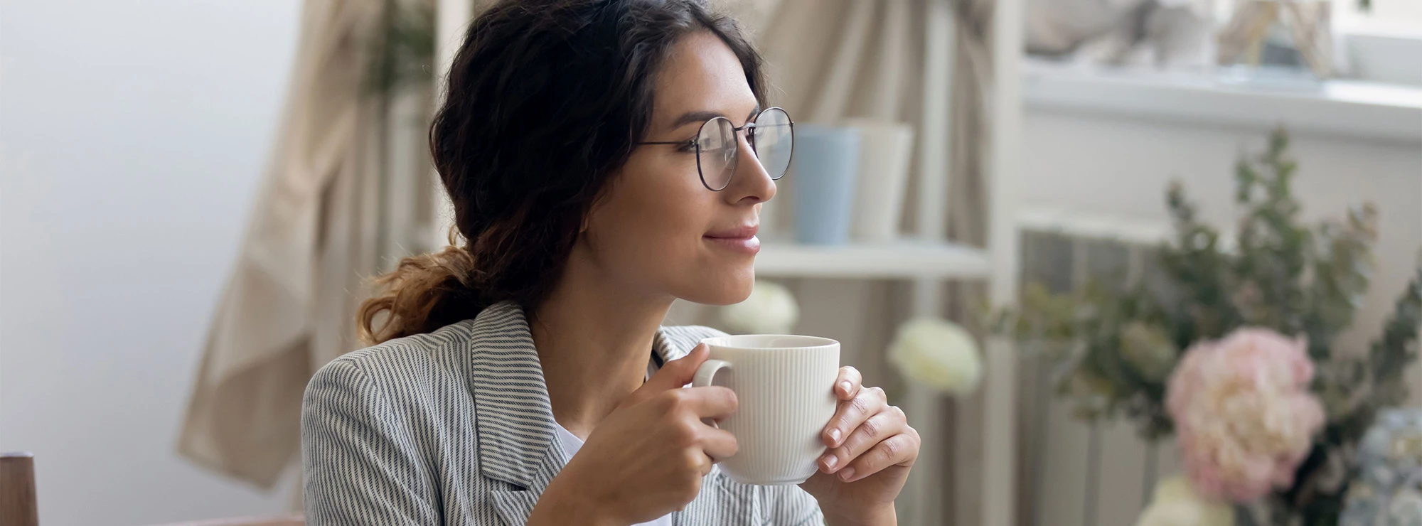 Smiling young business woman with glasses drinks coffee at home in her office