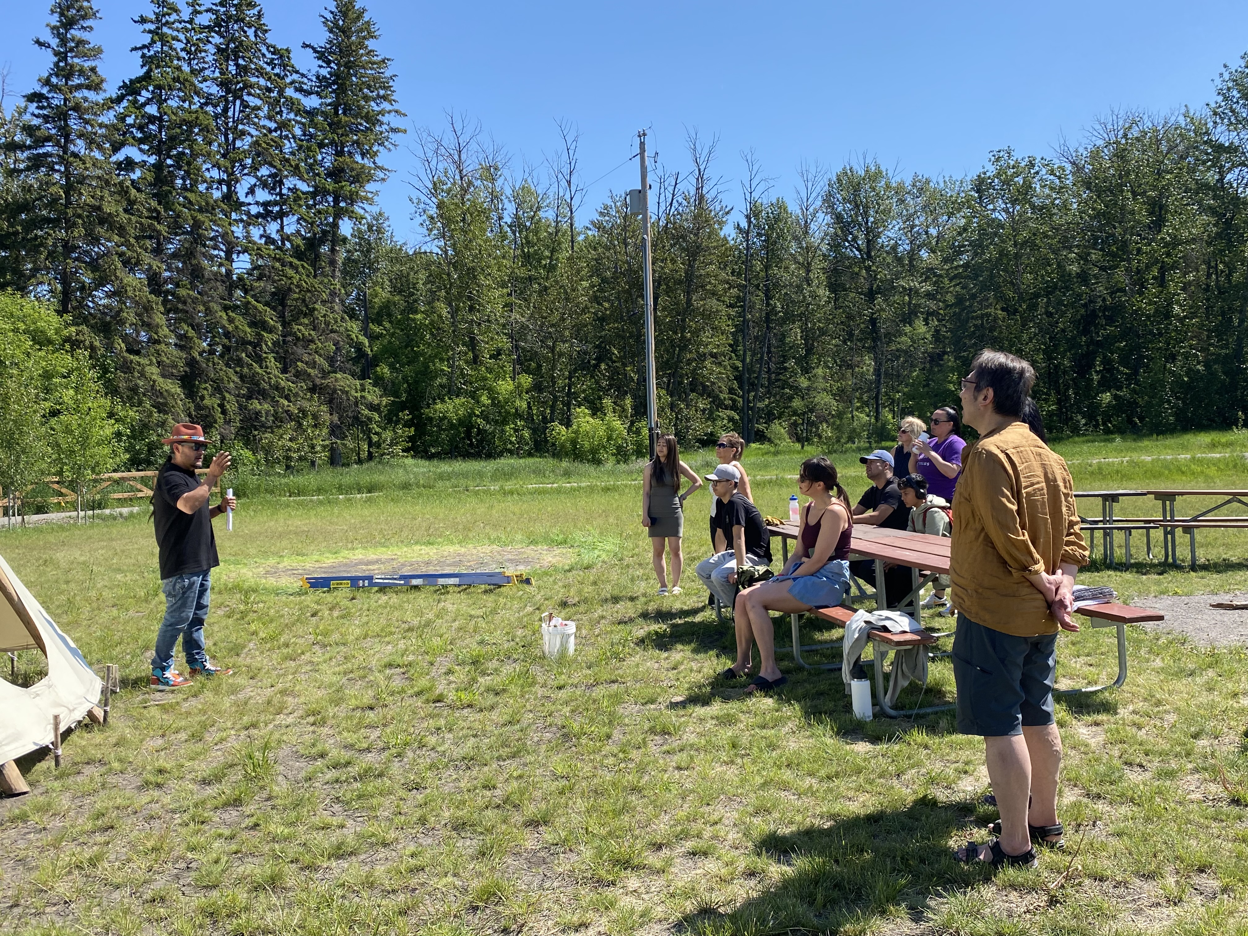 Larson Yellowbird partageant des enseignements sur le tipi avec les membres de l’équipe TELUS à l’extérieur, sur un terrain dégagé.

