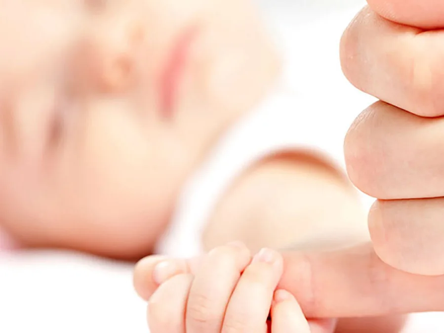 Closeup of a premature baby grasping someone’s pinkie finger