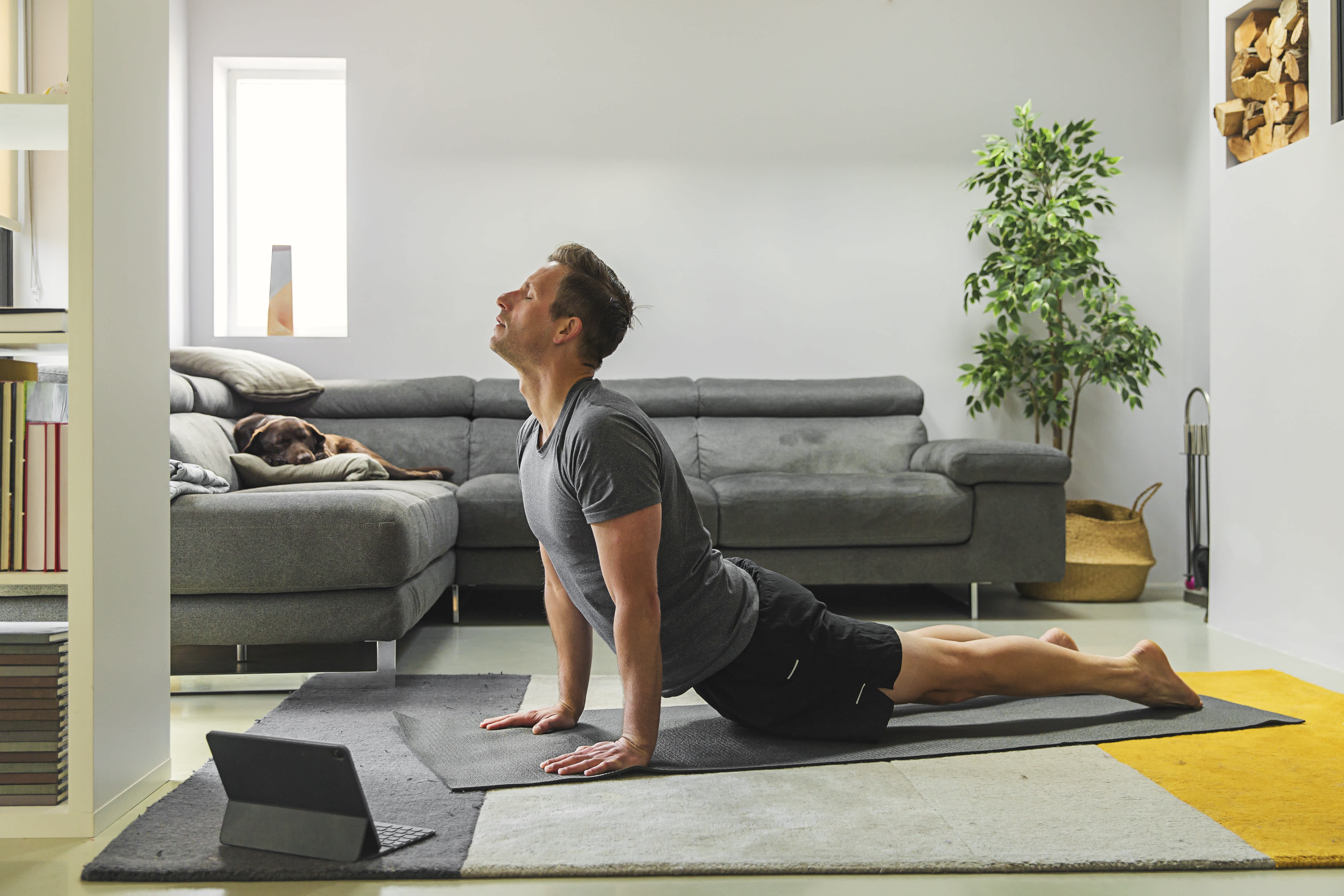 Man in his living room attending virtual yoga class practicing yoga poses to improve his sleep quality.