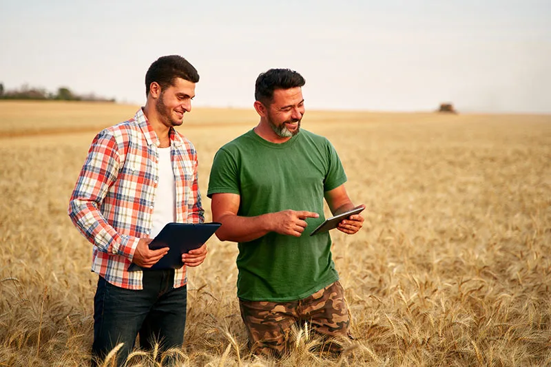 Two men standing in a field smiling and looking at an tablet.