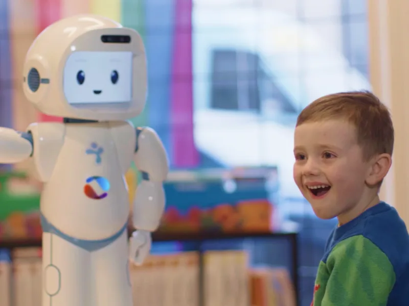 Preschool age child in a Learning Disabilities Society program engaging with a social robot. 