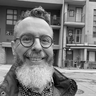 Person with a beard and glasses standing in front of a building