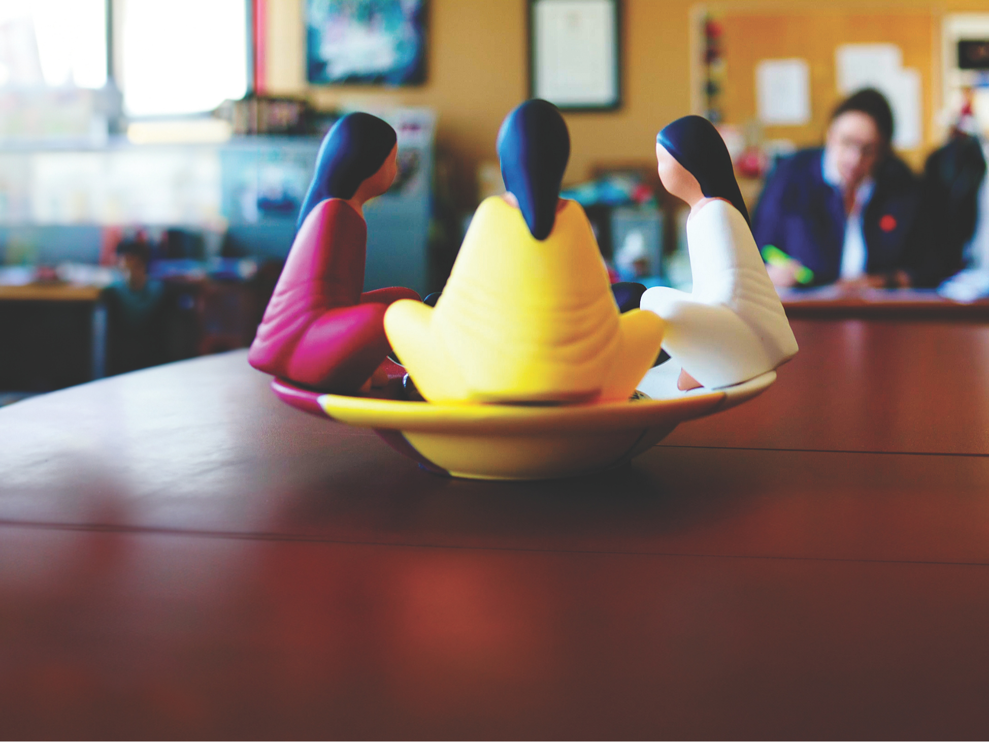 Gros plan de trois figurines sur un bureau représentant des femmes assises en tailleur en cercle.

