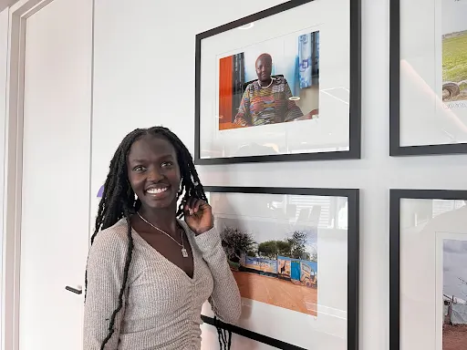 Grace at the TELUS office smiling with photos from the Kakuma refugee camp beside her.