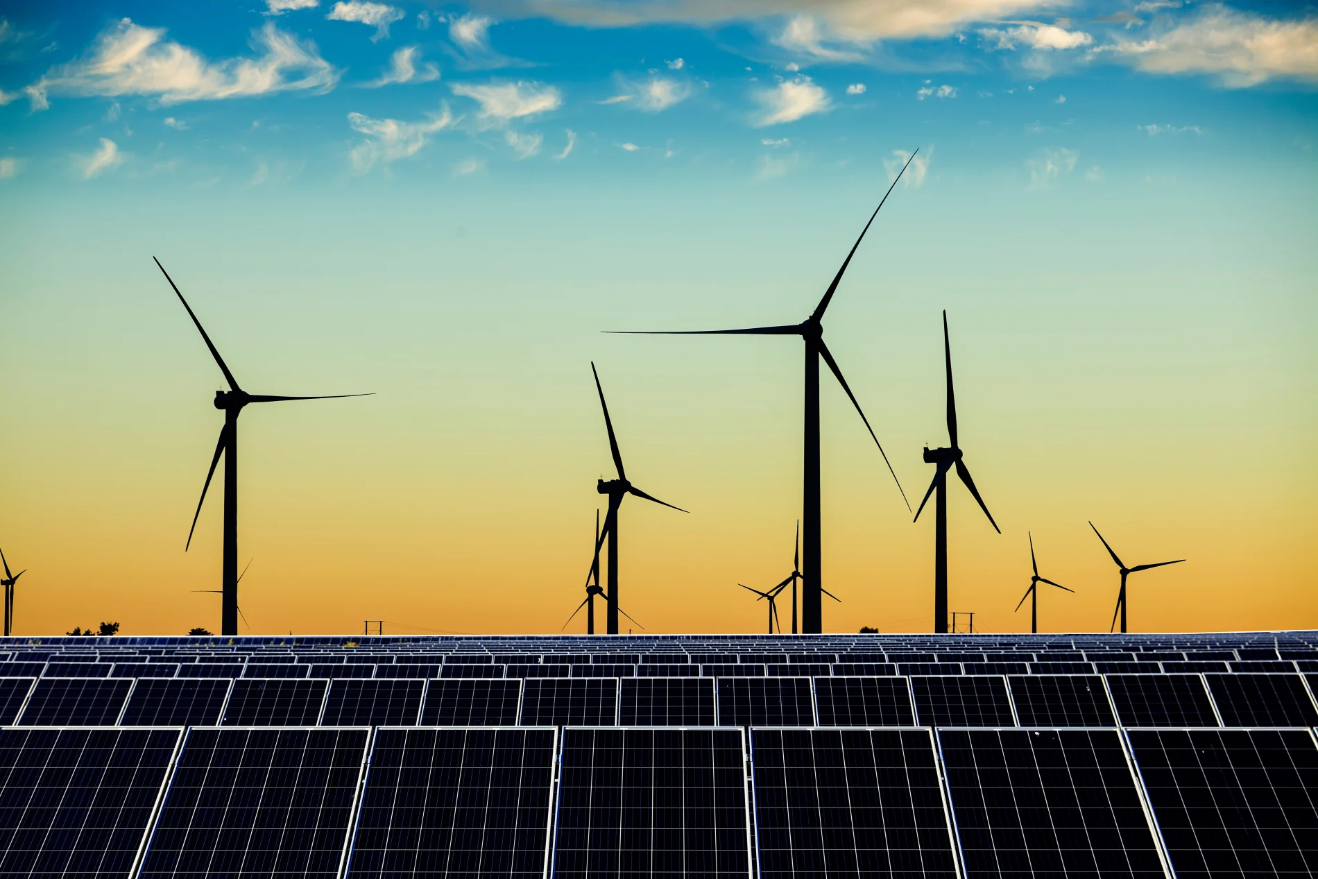 solar panels and wind turbines against a blue and orange sky