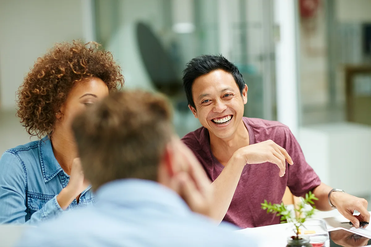 Three people sitting around a table, focus is on one man who is laughing