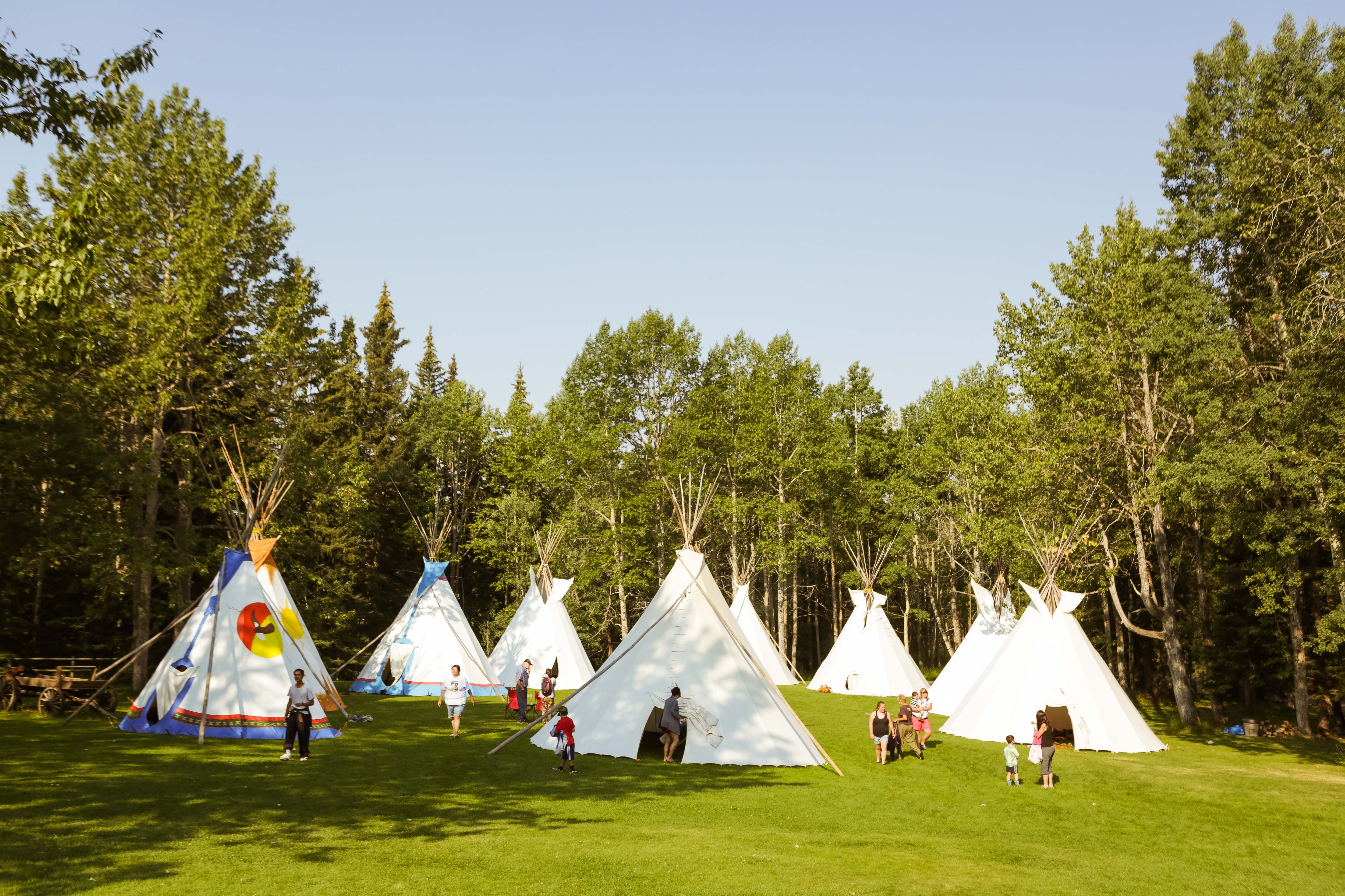 Des jeunes autochtones et leurs familles rassemblés près de tipis dans un camp culturel en nature.