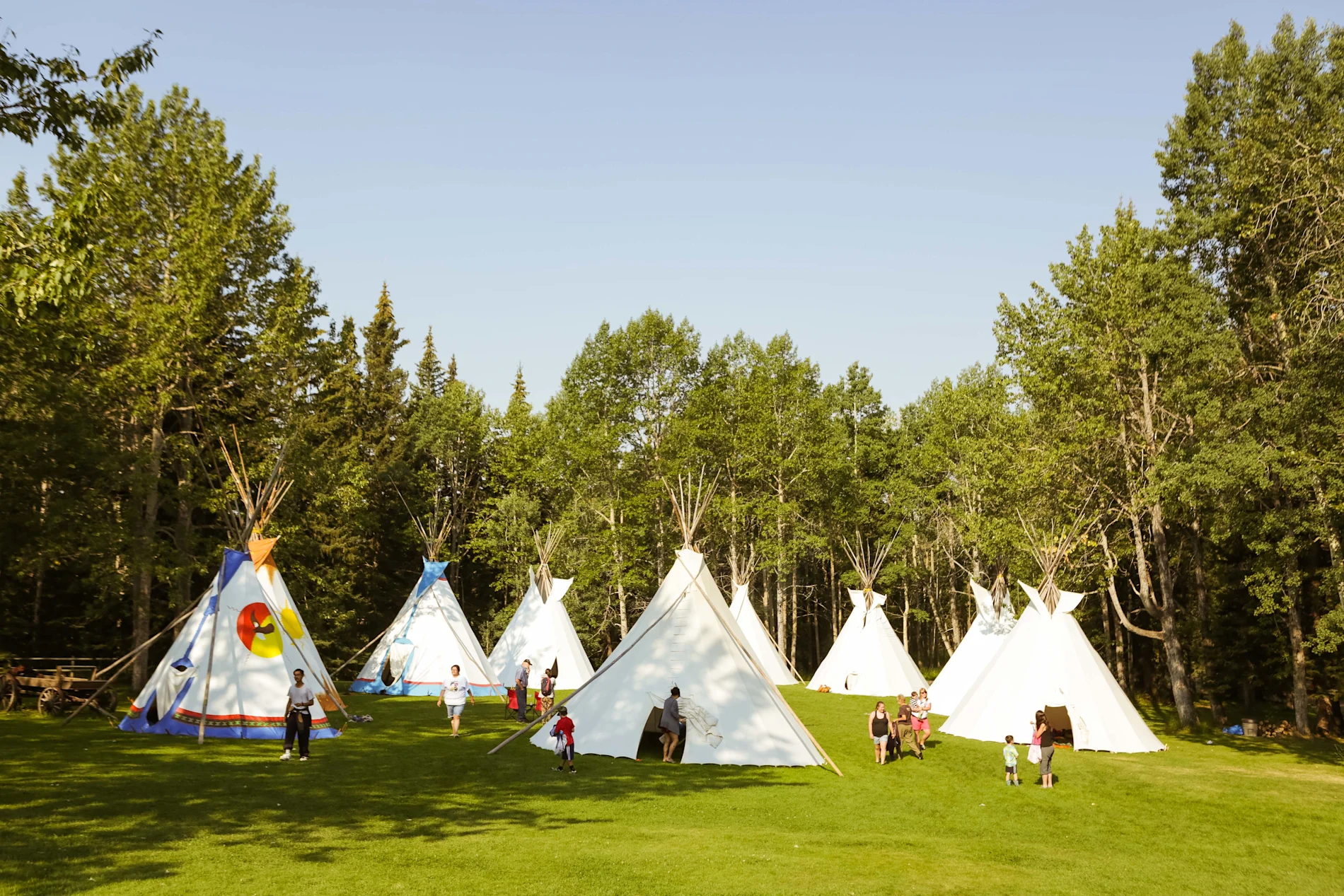 Des jeunes autochtones et leurs familles rassemblés près de tipis dans un camp culturel en nature.