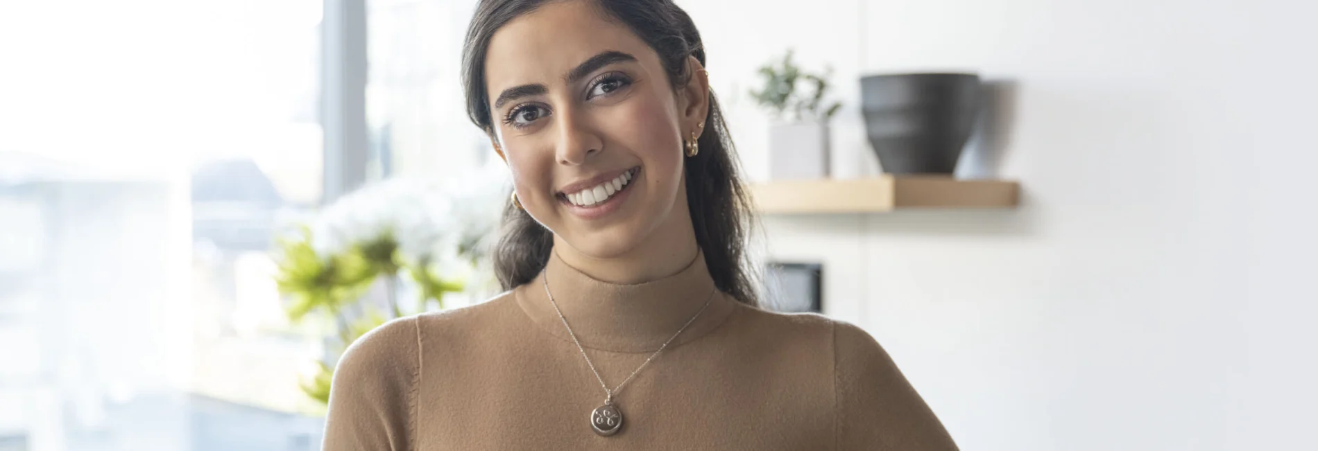 A young woman, smiling, and wearing a TELUS SMartWear Security necklace