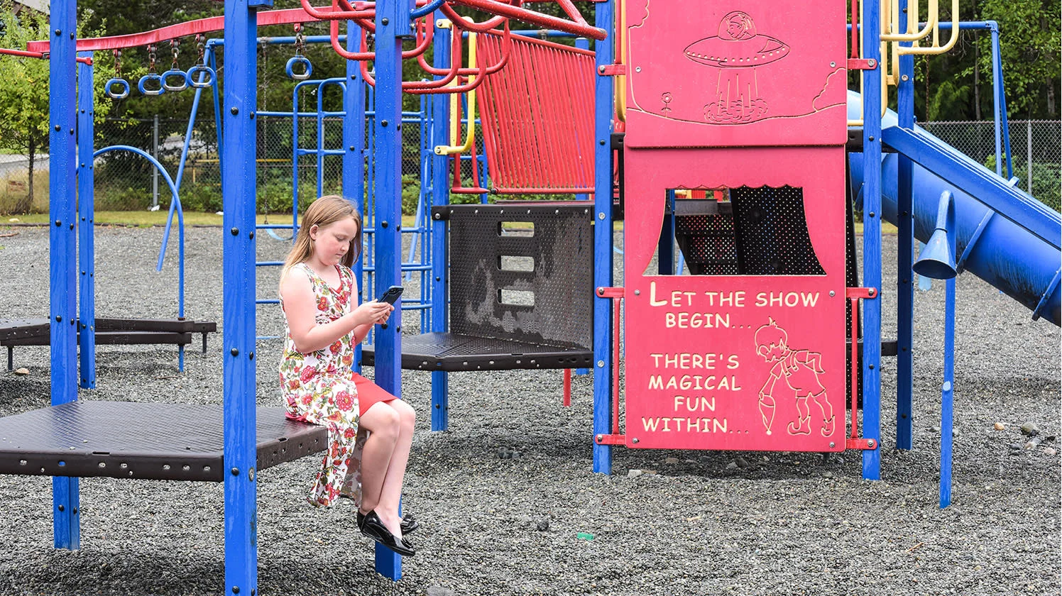 A child looking at a cell phone in a playground.