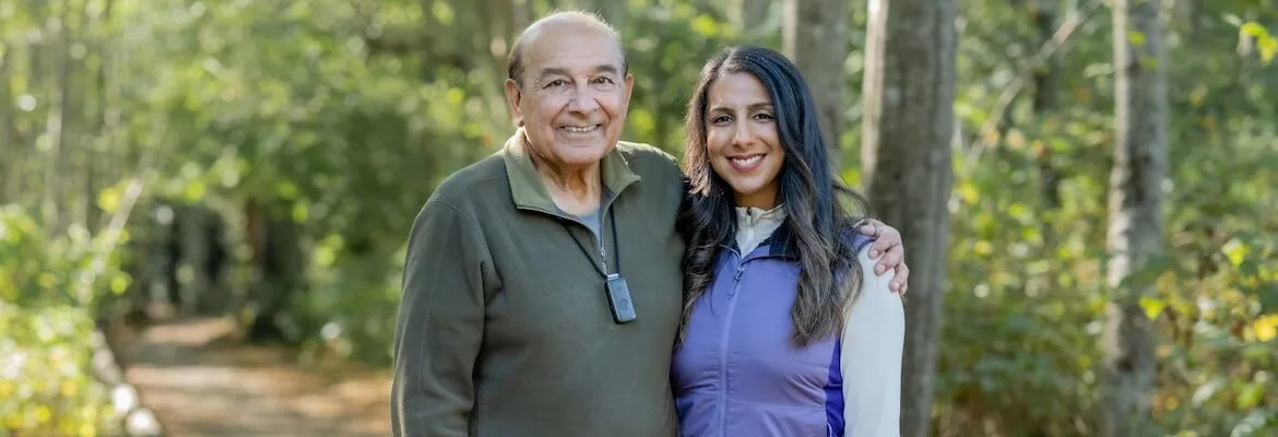 An elderly man and his daughter smile together on a wooded trail. He wears a discreet emergency pendant, demonstrating how medical alert systems for seniors Canada provide peace of mind and safety for active families enjoying the outdoors.