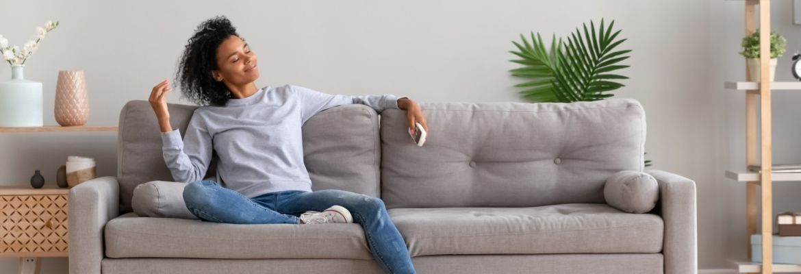Woman sitting on her couch happy because she's practicing self-love, taking care of her mental and physical well-being.