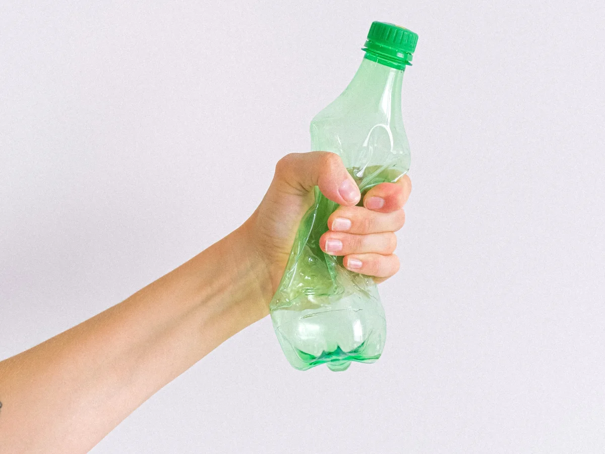 An outstretched hand tightly holding a green plastic bottle
