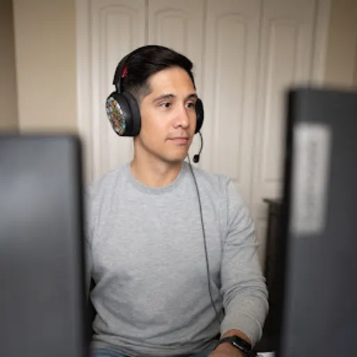 Male with dark hair, with a headset on looking at computer screens. 