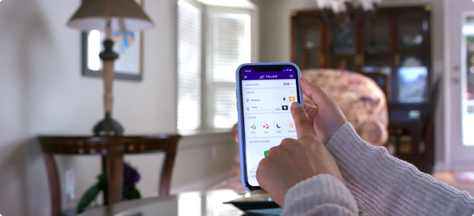 A person holding their smart phone, using their finger to control the lighting thanks to their TELUS SmartHome Security and Automation system.
