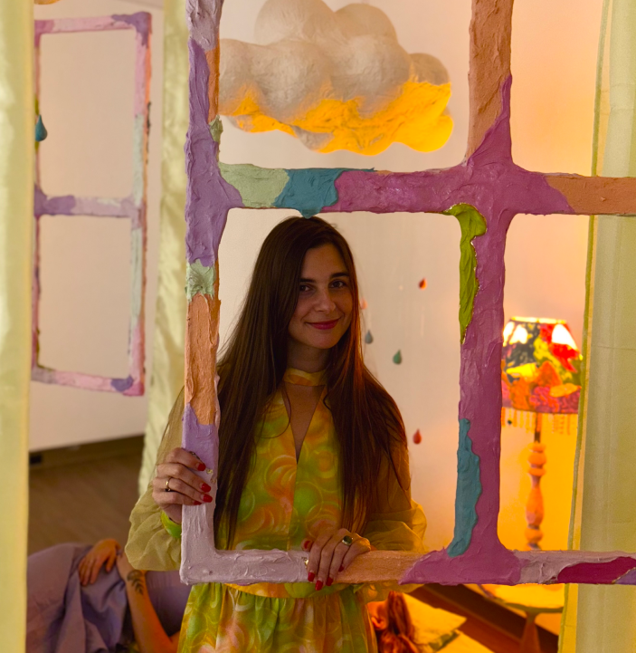 Red River Métis artist Morgan posing behind a colorful sculpted window frame.
