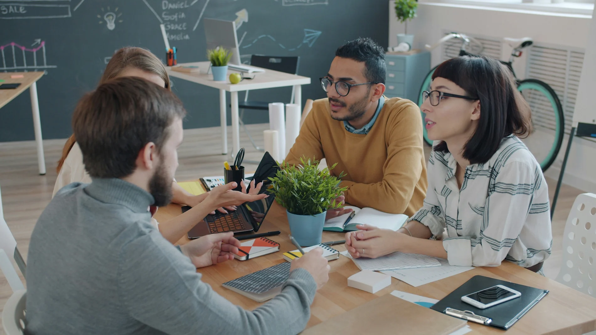 Four professionals having a discussion around a table, with one person using a laptop.