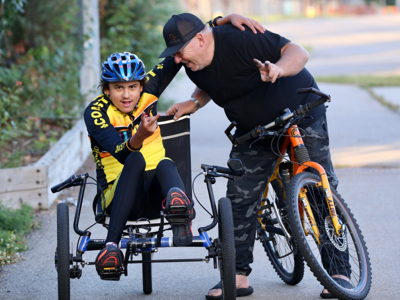 Un jeune homme présentant un handicap physique fait du vélo à côté de son instructeur.