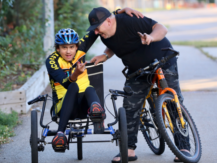 A male youth with a physical disability riding a bike alongside his instructor.