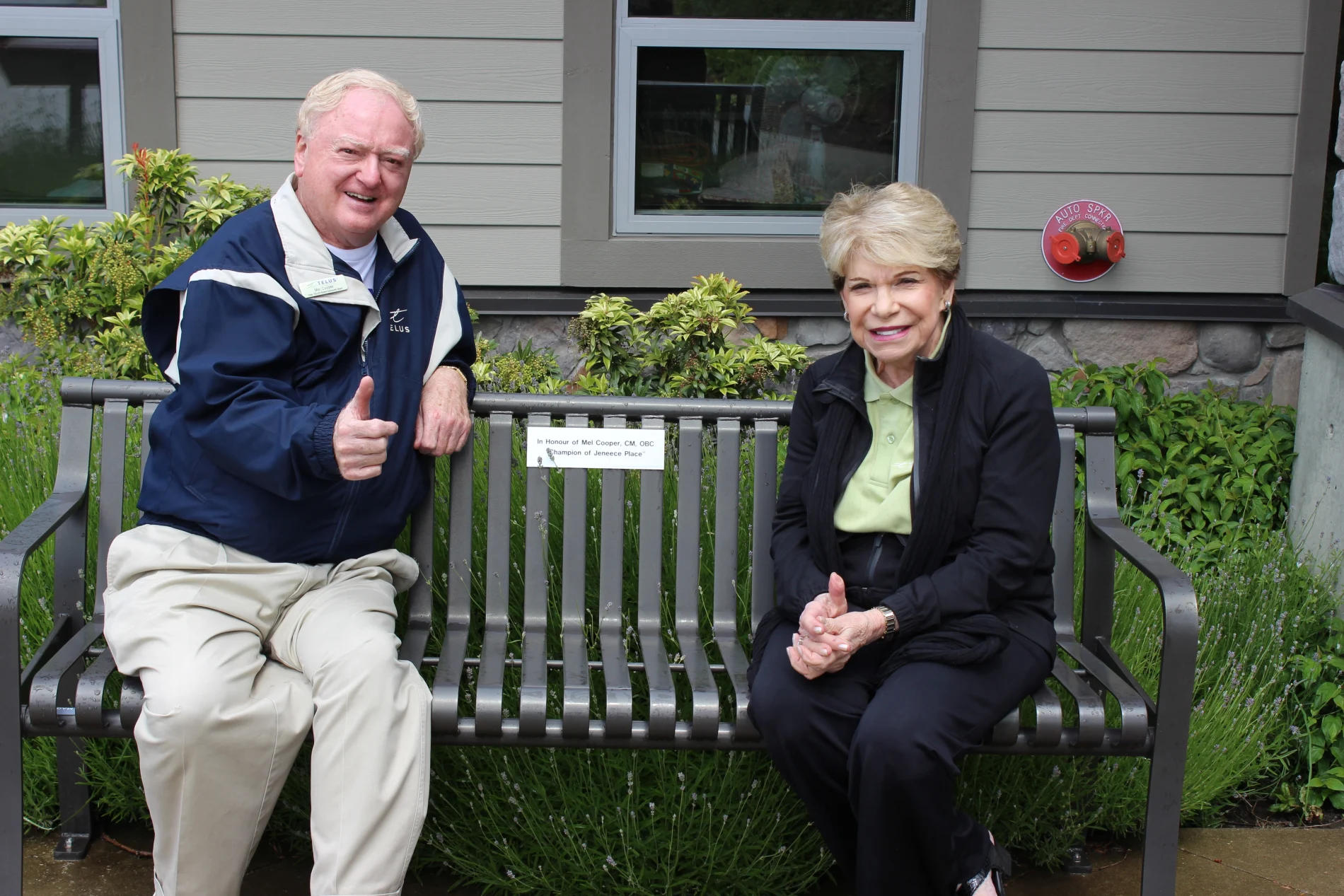 Mel Cooper, Chair Emeritus of the TELUS Vancouver Island Community Board, and his wife, Carmela sitting on a bench in front of Jeneece Place.