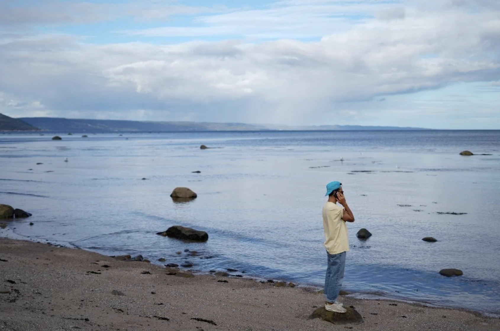 Person standing at the shoreline, talking on a mobile device