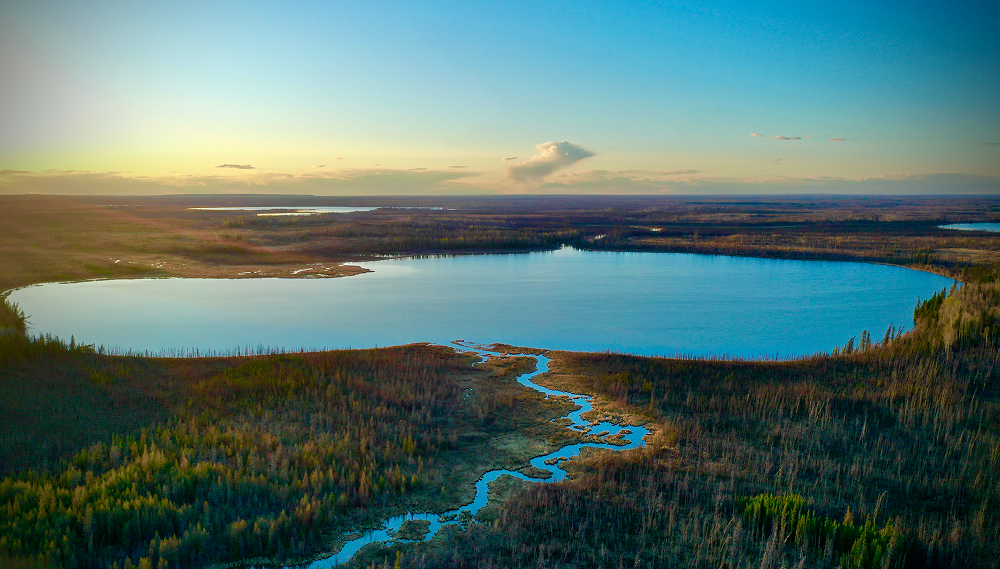 Aerial view of a winding river flowing into a large blue lake surrounded by vast green forest at sunset.