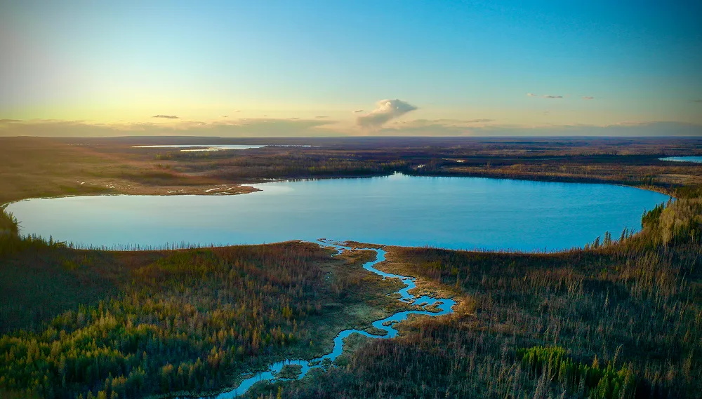 Aerial view of a winding river flowing into a large blue lake surrounded by vast green forest at sunset.