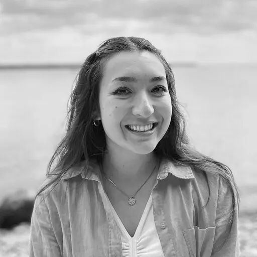 A person with long hair smiling in front of a body of water