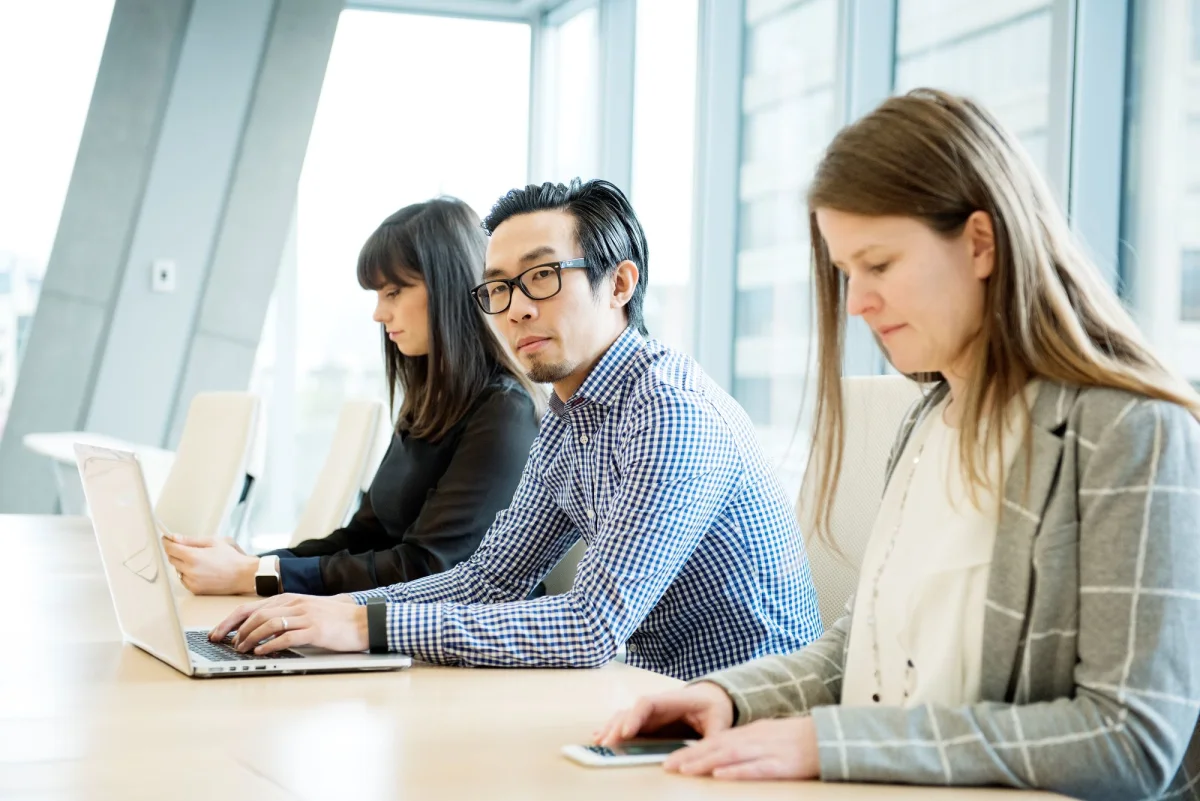 Trois collègues au bureau qui travaillent à l’ordinateur ou au téléphone.