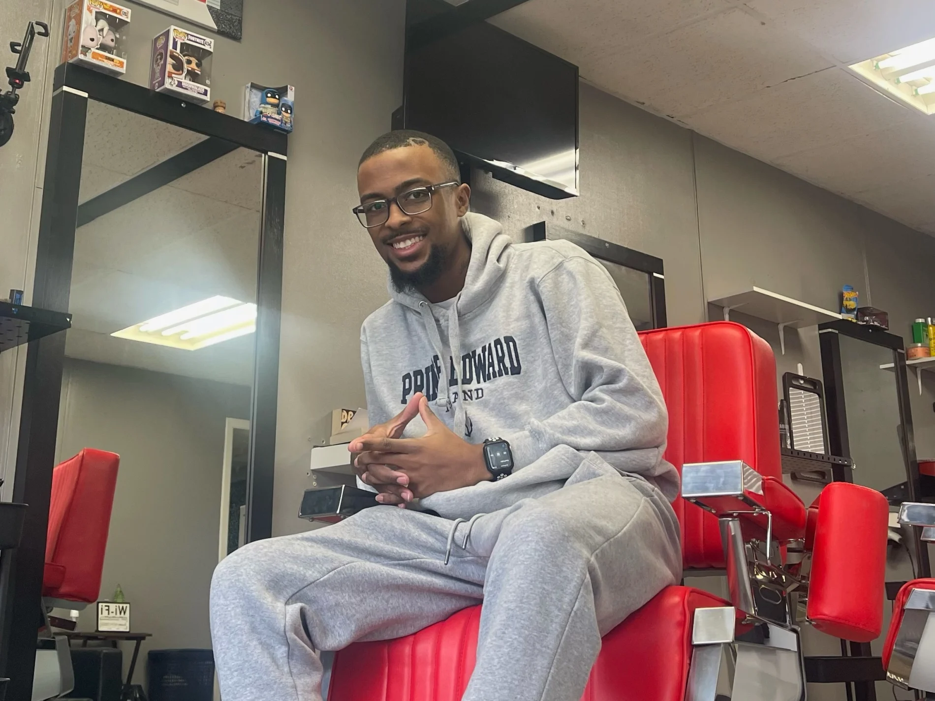 Perrier, former student in the Bartley Skills Development Program in Beyond Barbering sitting in a barber chair at the barber shop he owns. 