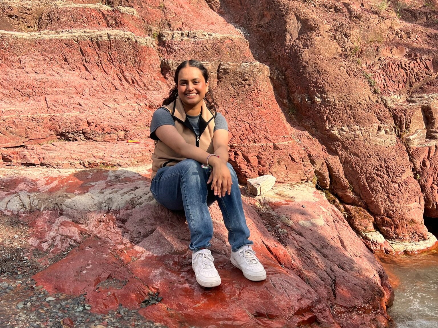 TELUS Student Bursary recipient, Sofia Sejutee sitting on a rock with a smile on her face. 