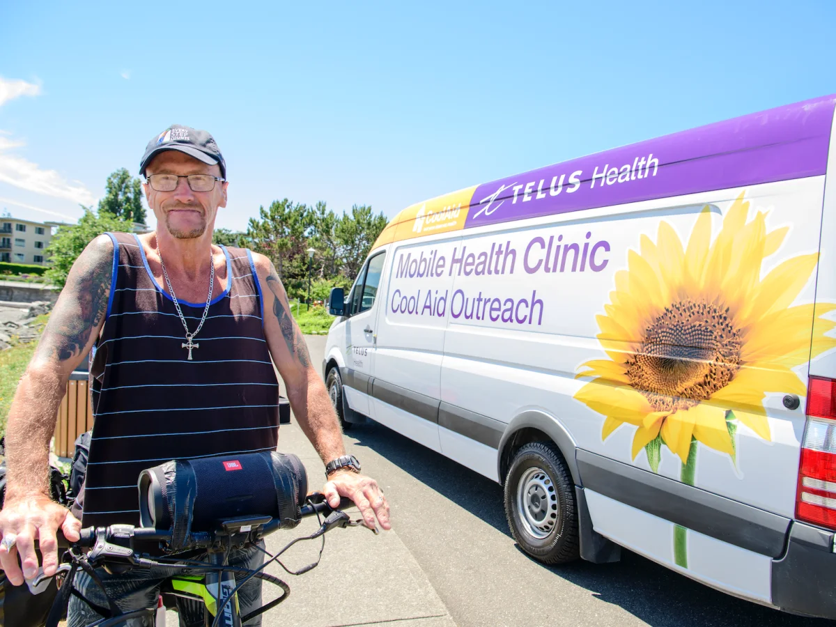 Un homme sur un bicycle sur le bord de la route et à coté d'un véhicule d'une clinique mobile de TELUS. 