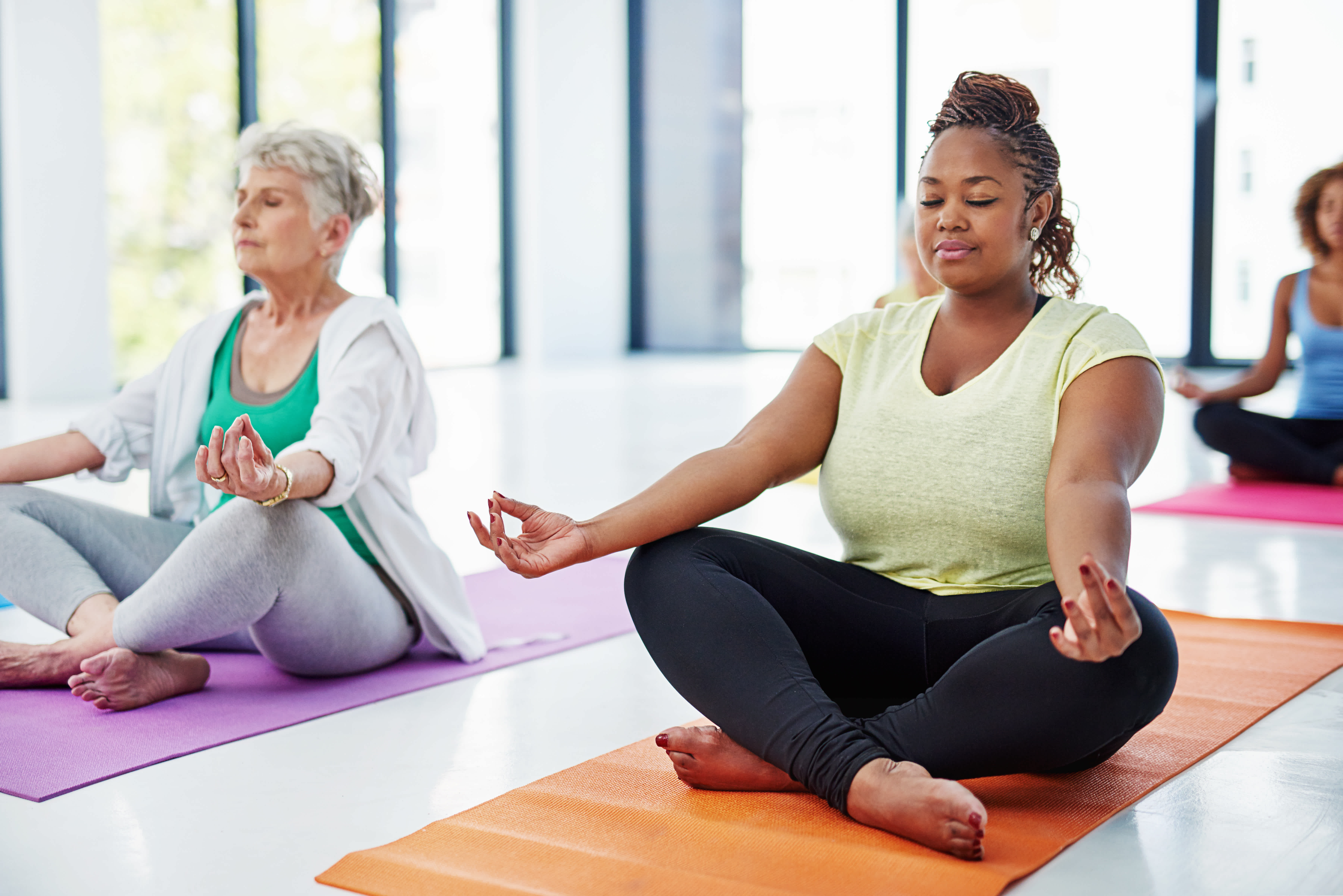 Two women meditating with their eyes closed and sitting cross-legged on yoga mats.