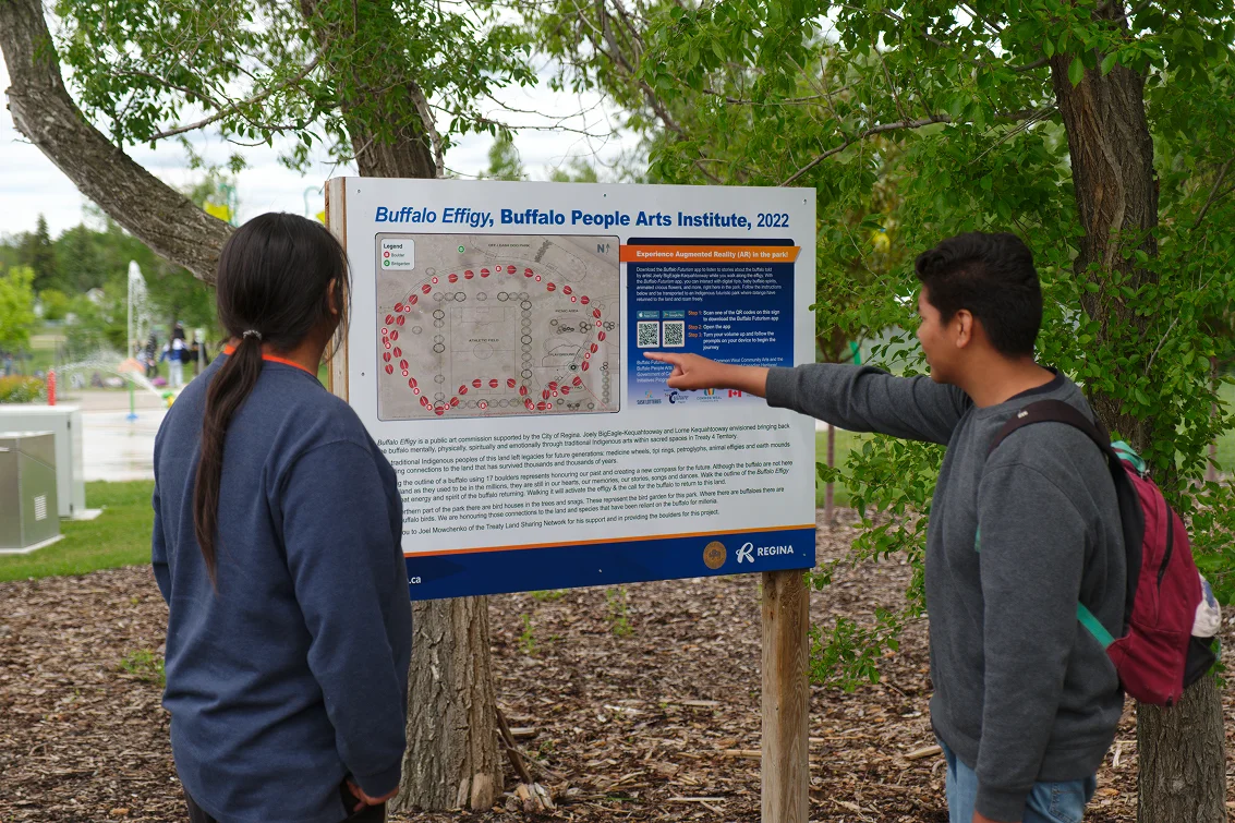 Deux adolescents lisent une pancarte dans un parc au sujet du Buffalo People Arts Institute