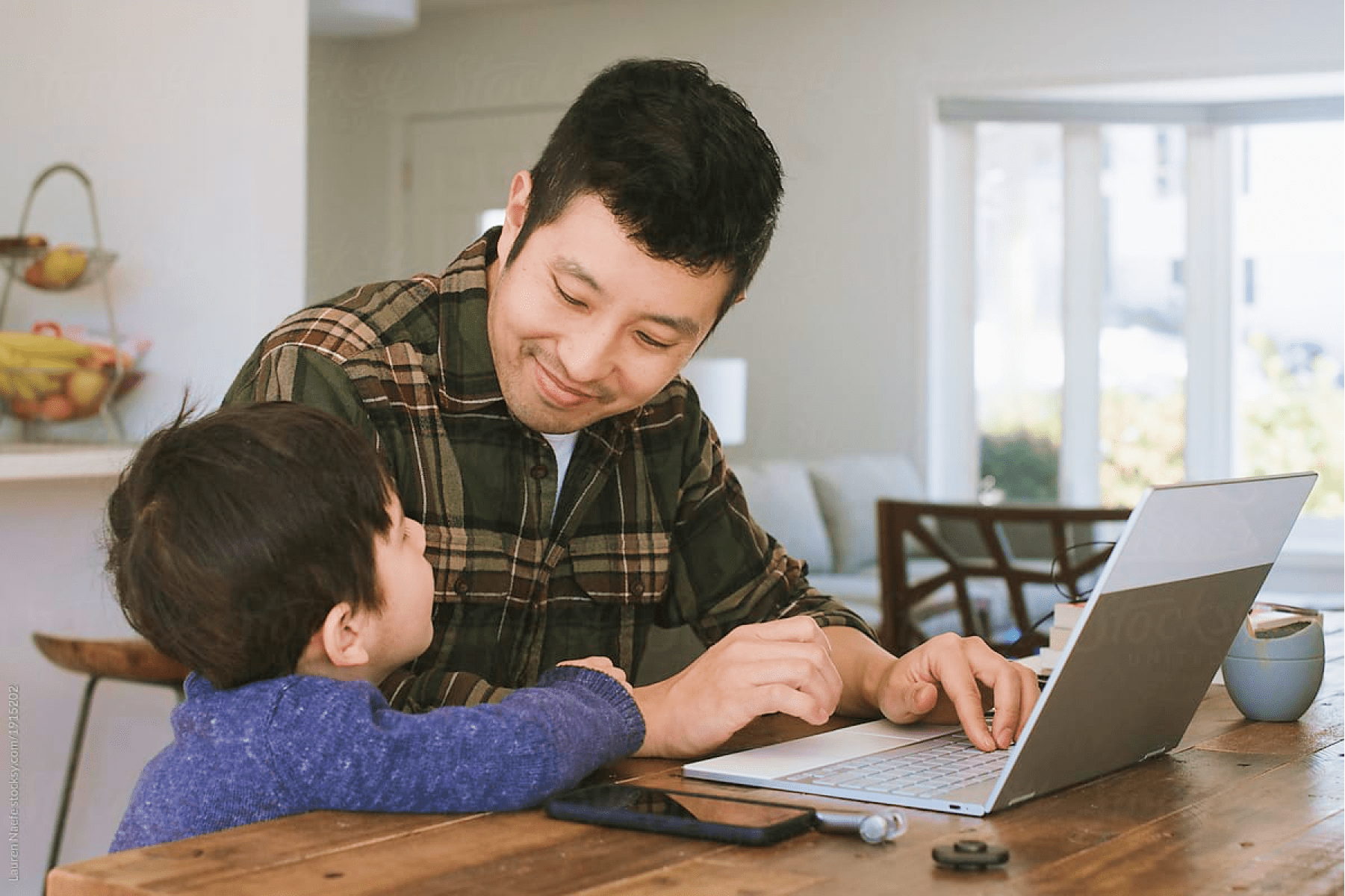 A father sitting in front of his laptop and smiling at his son.
