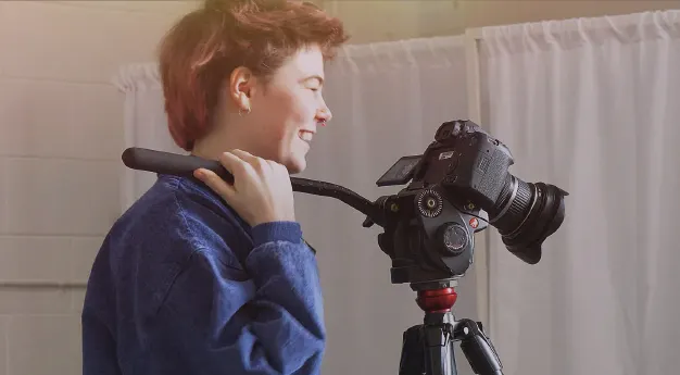 A content creator standing next to a camera on a tripod.