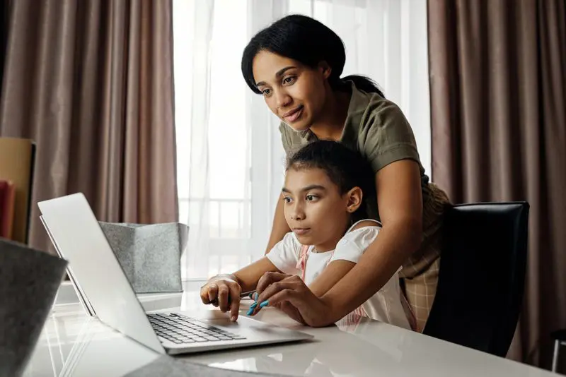 Mother helps child student with work at computer.