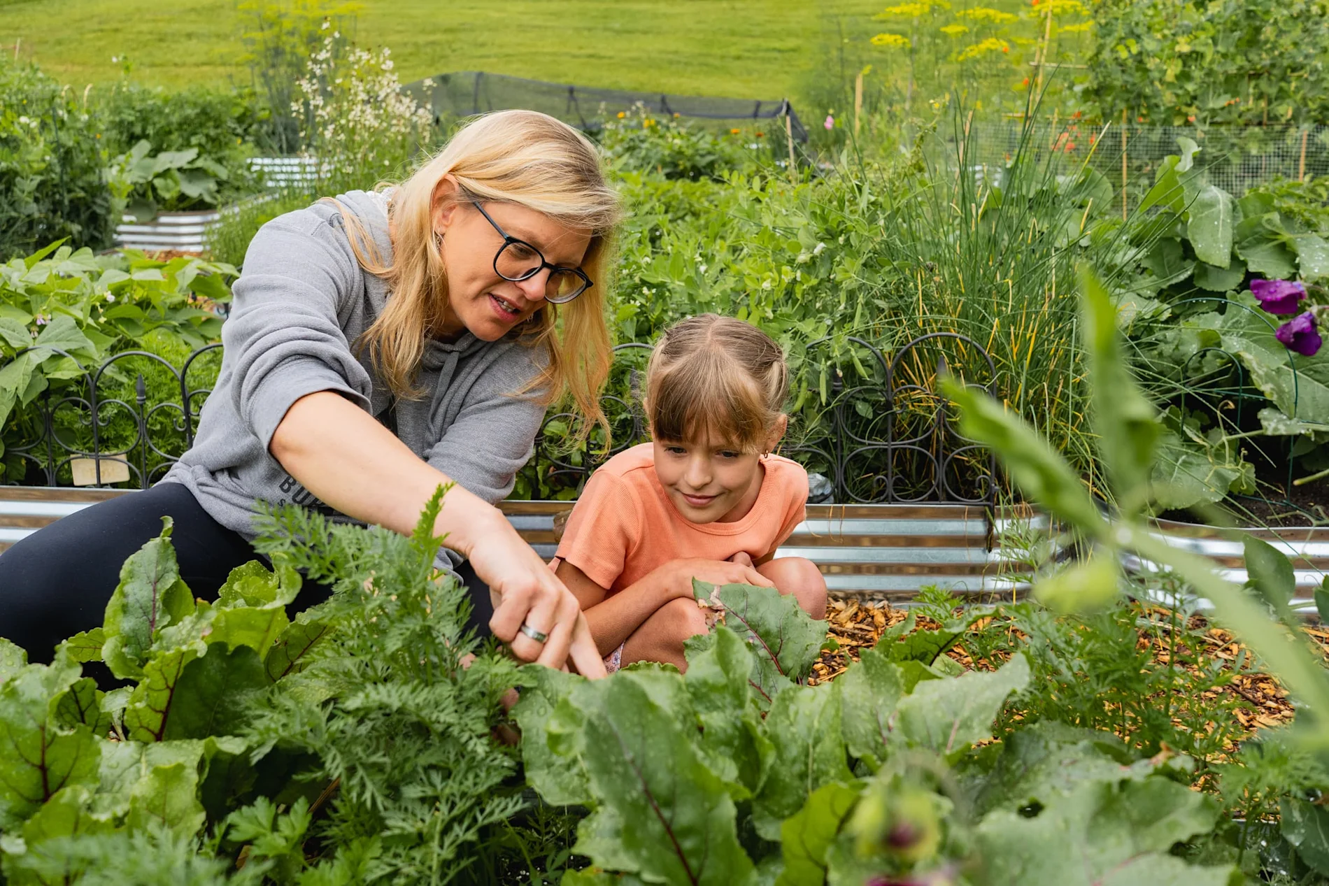 Female mentor and mentee exploring vegetables in a garden.