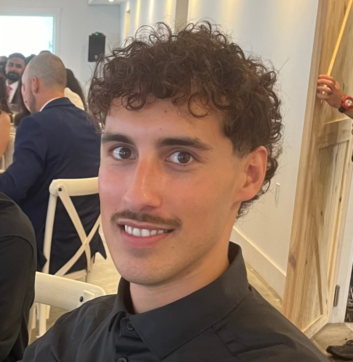 A photo of Israel at an event sitting down, looking at the camera.