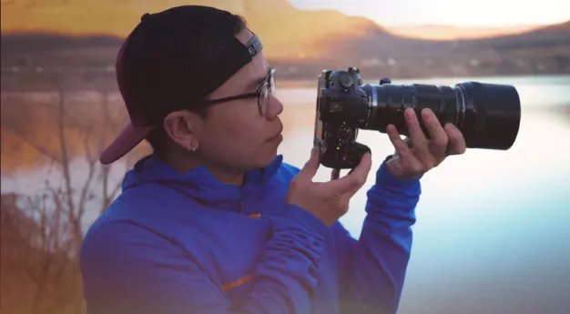 A content creator standing by the river and holding a camera.