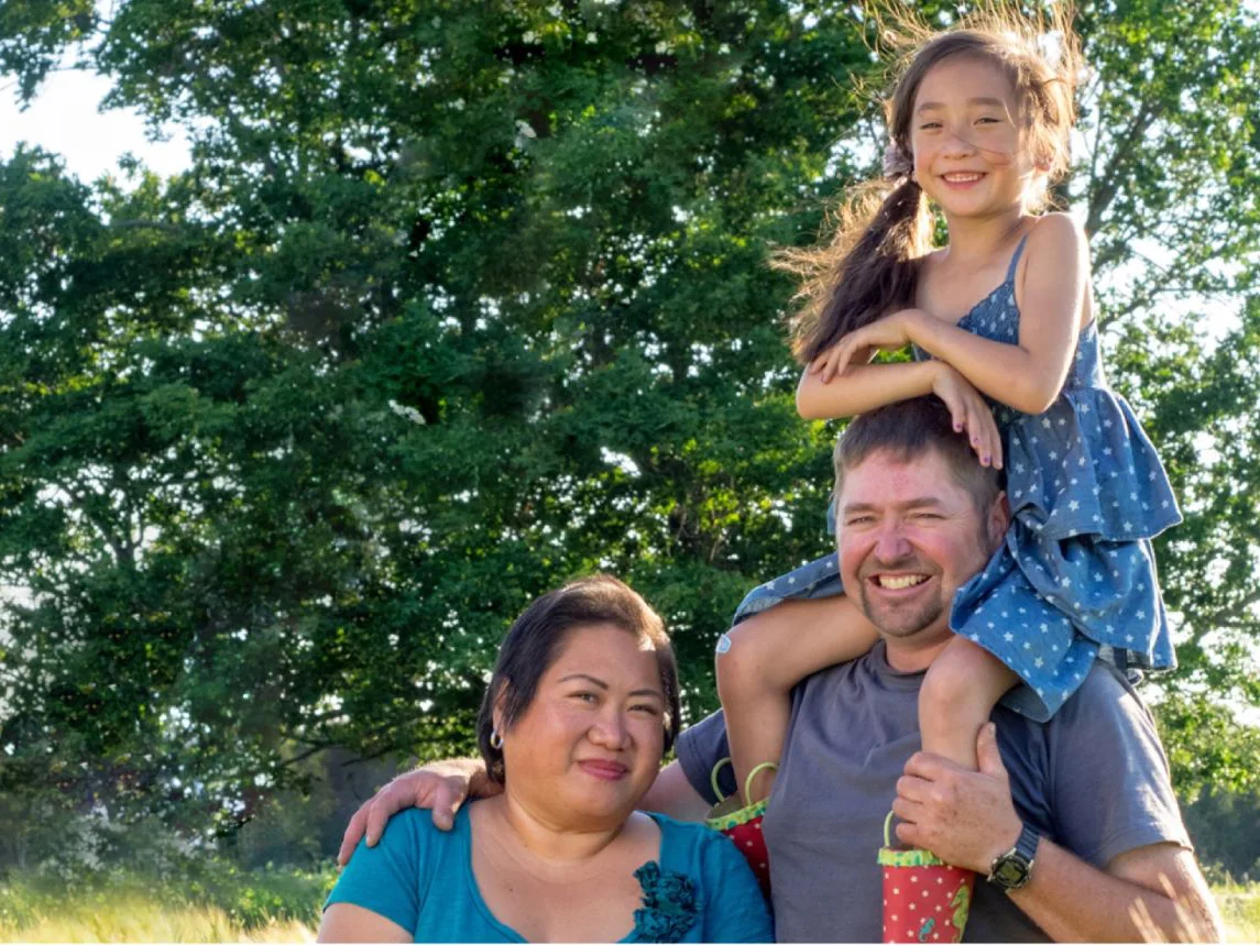 Christine McNaughton posing beneath a tree with her husband and daughter, Lola